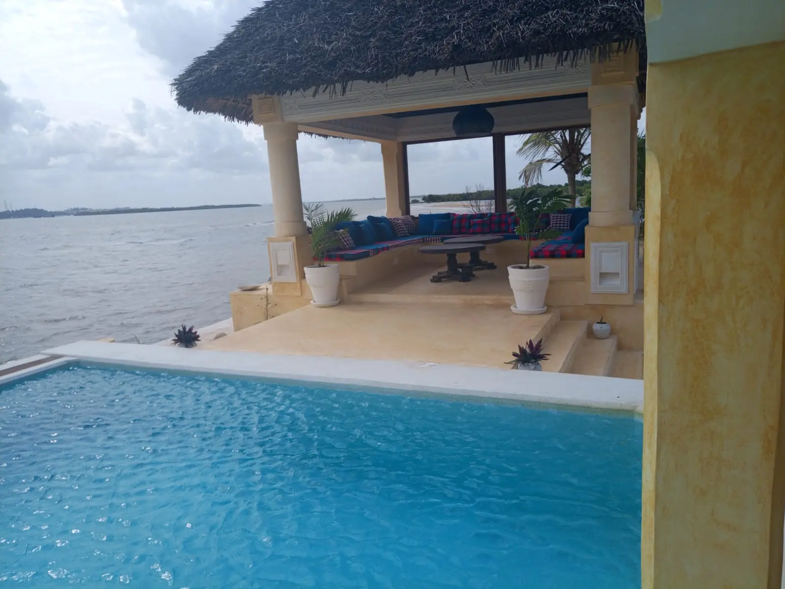 Thatched roof pavilion by pool with blue cushioned seating and ocean views